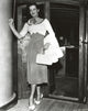 Jane Russell posed in a scoop-neck long sleeve dress with polka dot high waist skirt holding a white handbag.