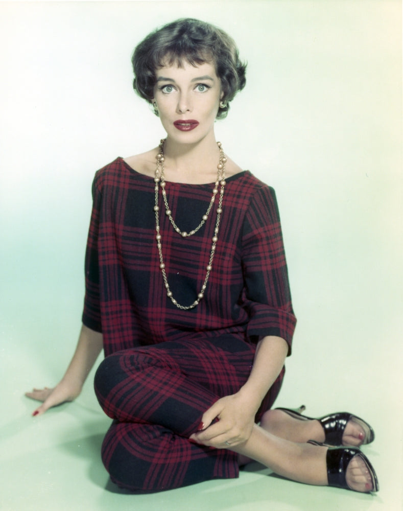 Phyllis Kirk seated on the floor in a red checkered dress portrait with a white background.