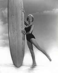 Janet Leigh posing in a black linen swimsuit holding a surfboard photo print