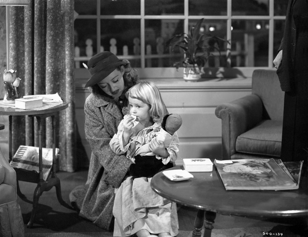 Bette Davis seated in black hat and cotton coat holding a child in white silk shirt photo print.