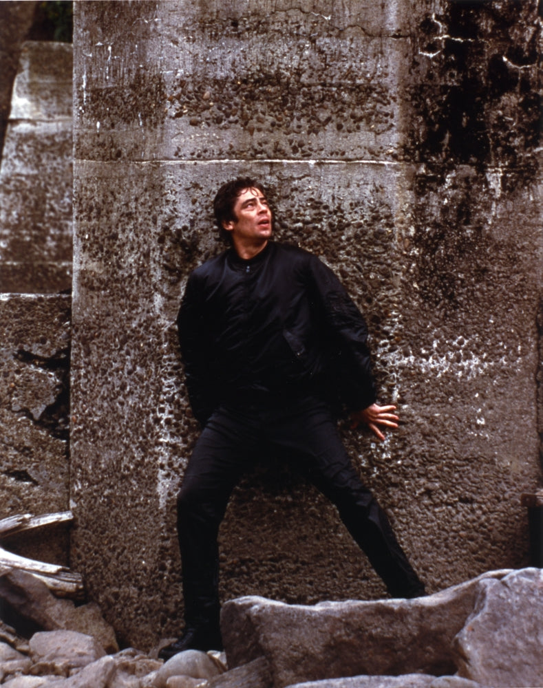 Benicio Del Toro leaning on wall in black coat photo print.