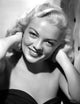Myrna Dell smiling in a black and white portrait photo print, hands on neck.