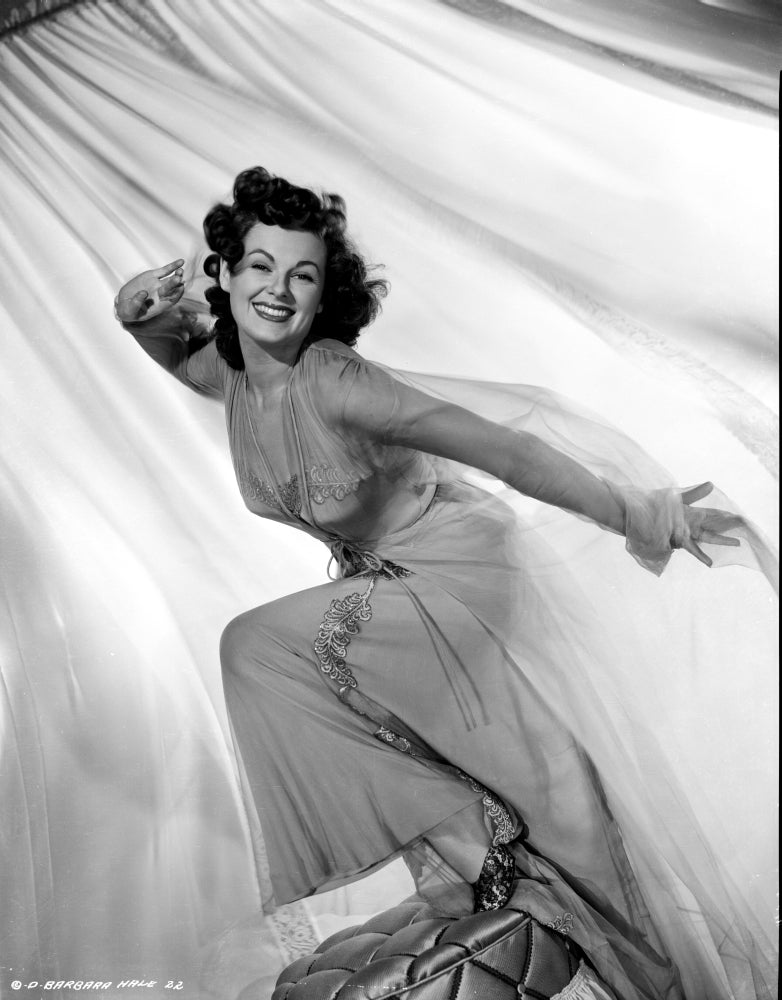 Barbara Hale in a lace dress posing elegantly on a chair.