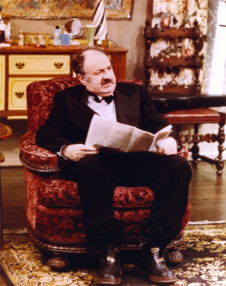Lou Jacobi sitting in chair with newspaper photo print
