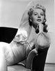 Irene Manning seated on a couch, vintage photo print.