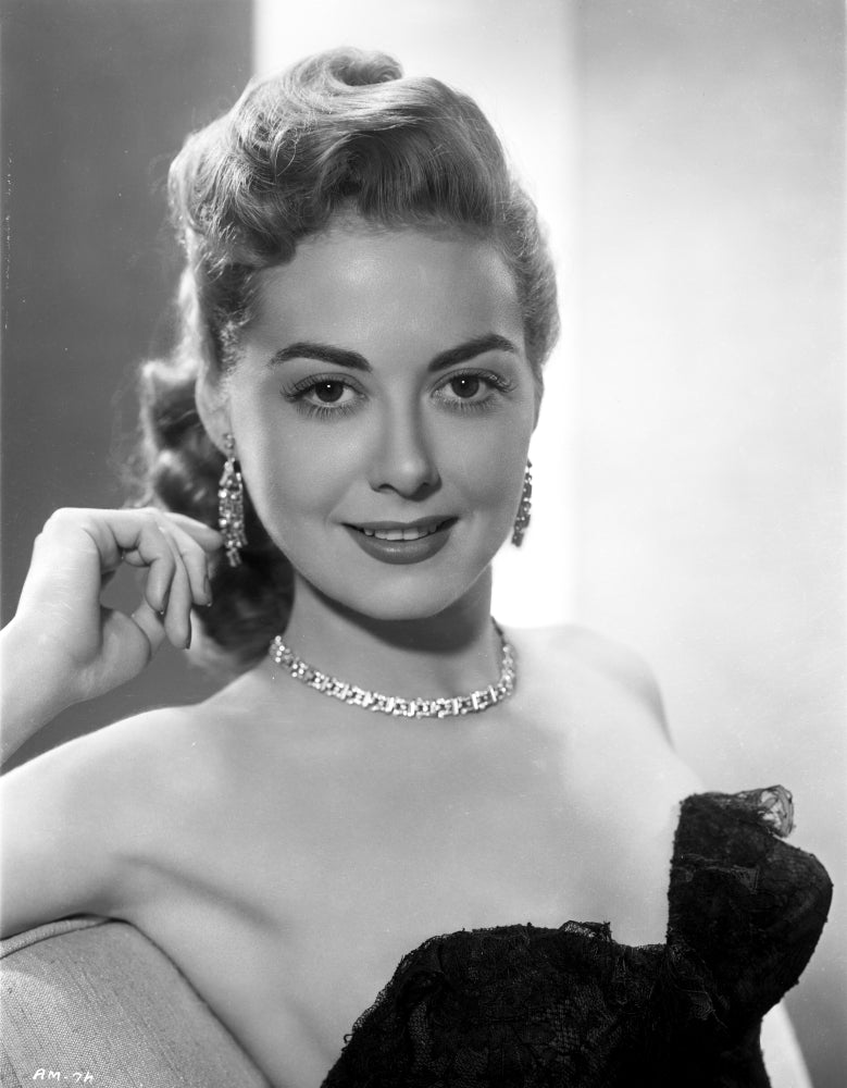 Adele Mara posed elegantly in a black dress with jewelry and a smile.