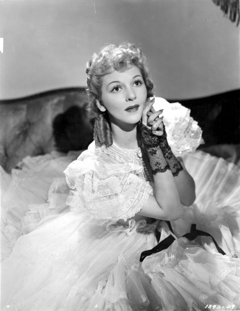 Mary Martin in a ruffled gown seated on a bed - Photo Print