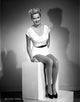 Photo print of Beverly Michaels seated in a white dress and black heels.