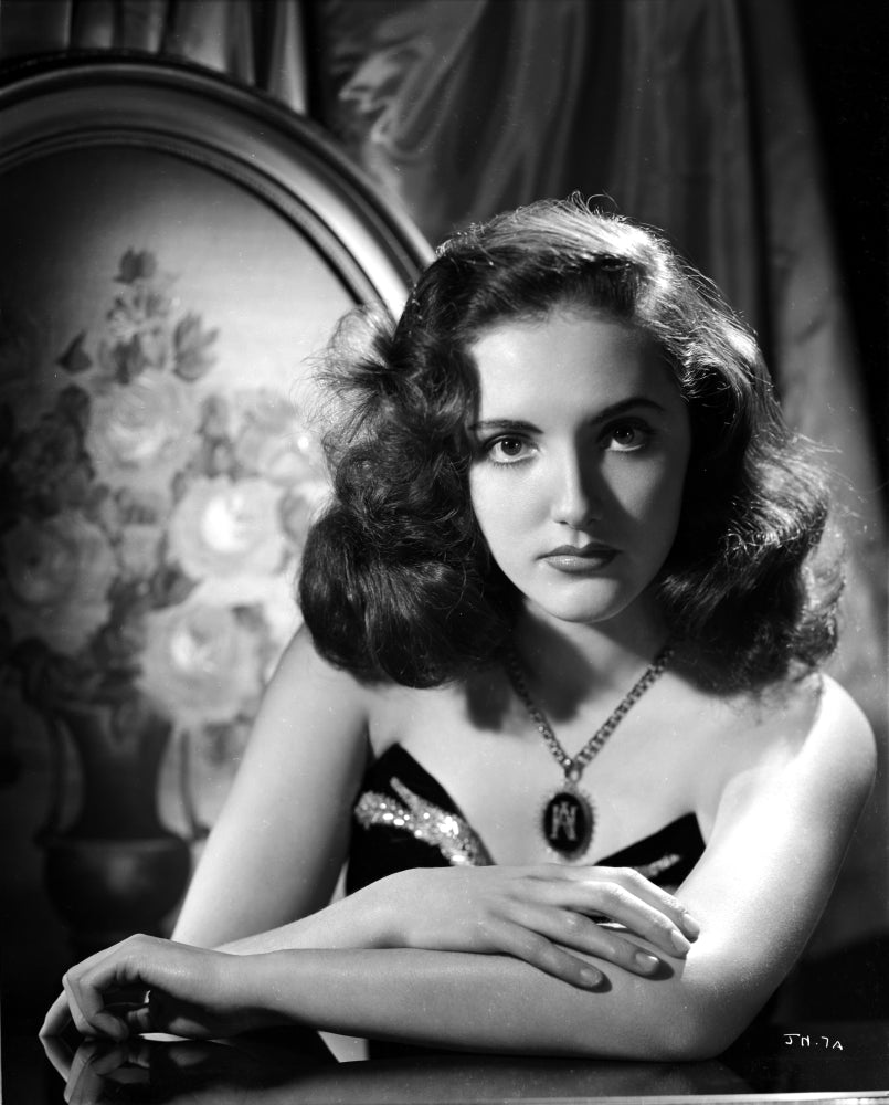 Portrait photo print of Joan Newton leaning on a table in a strapless black dress.