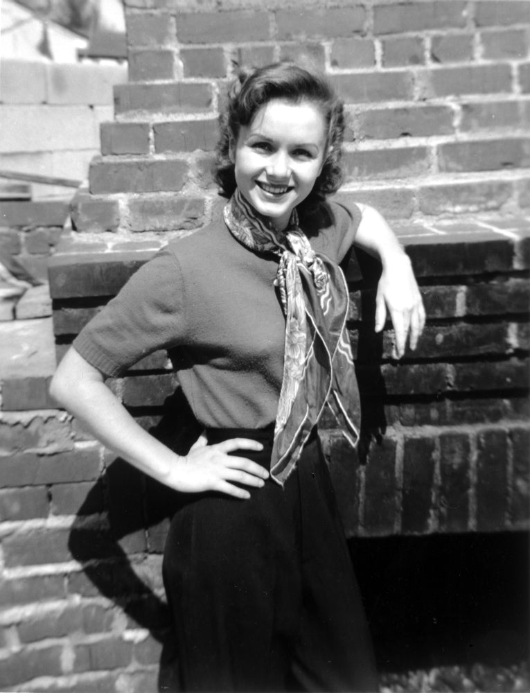 Debbie Reynolds leaning on bricks in a sweater with scarf photo print.