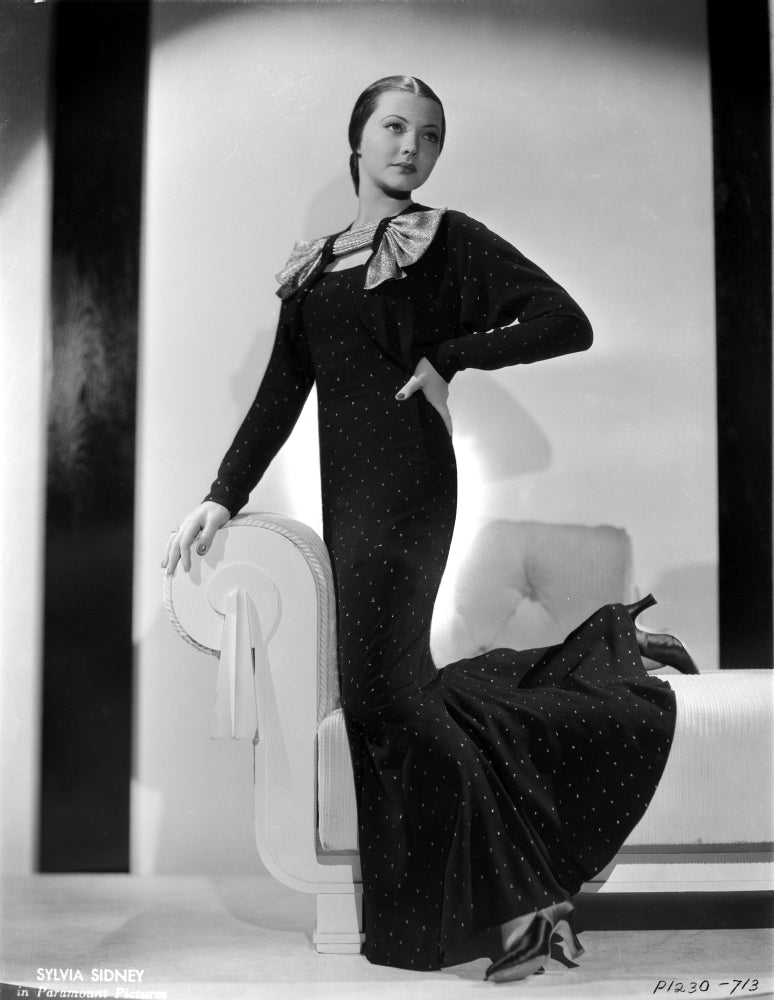 Sylvia Sidney posed elegantly on a white couch in a black long gown photo print.