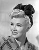 Close-up portrait photo print of Penny Singleton smiling with a flower headband.