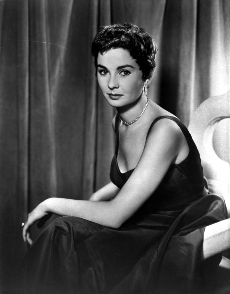 Jean Simmons seated on a couch in a black velvet strap dress photo print.