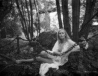 Veronica Carlson in a white chiffon ruffled robe, lying in the forest, holding a spiked chain link.