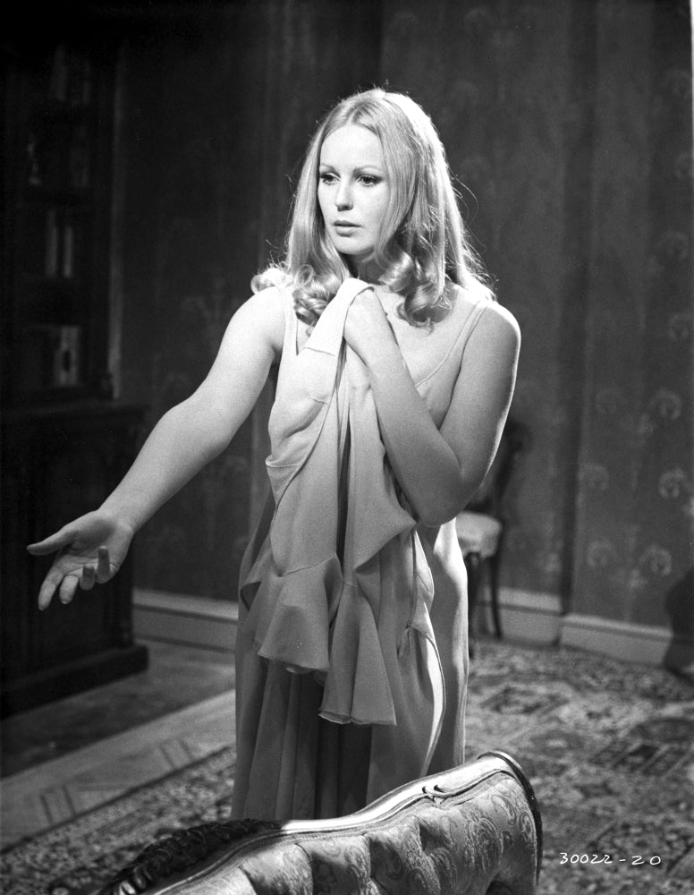 Veronica Carlson standing with arm raised and clutching a jacket photo print.