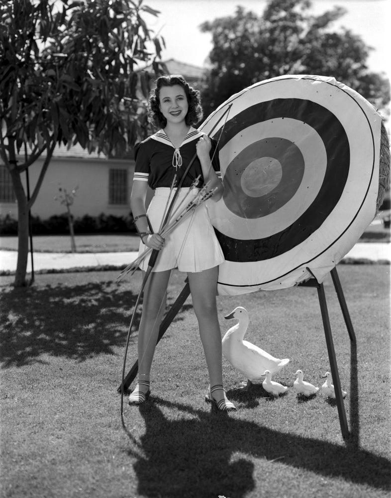 Jane Withers posing in a black short sleeve bodice with a bow and arrow photo print.