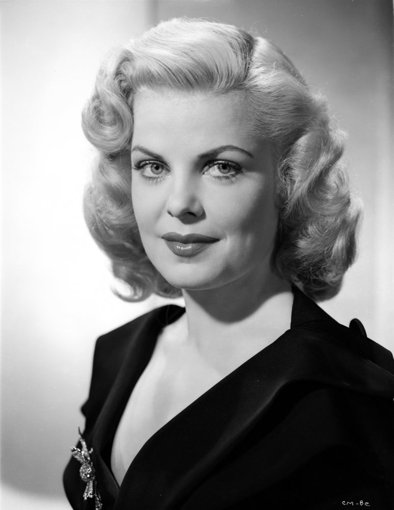 Cleo Moore posed in a black dress with a smile photo print.