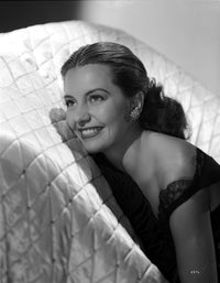 Cyd Charisse smiling on a white couch in a black sleeveless dress photo print.
