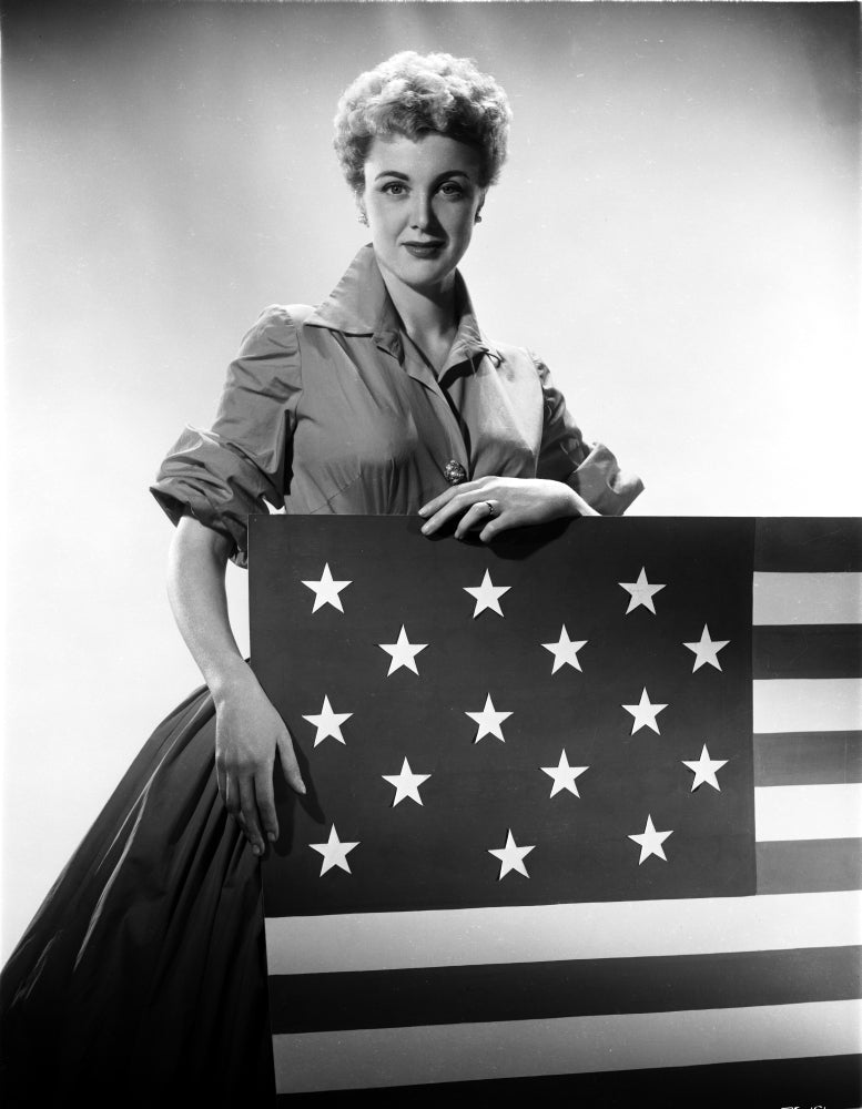 Jan Sterling photo print in velvet shirt and pleated skirt holding a flag.
