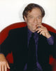 George Segal smiling while sitting on a red couch in a black suit photo print.