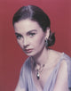Close-up portrait of Jean Simmons in grey linen dress with red background.