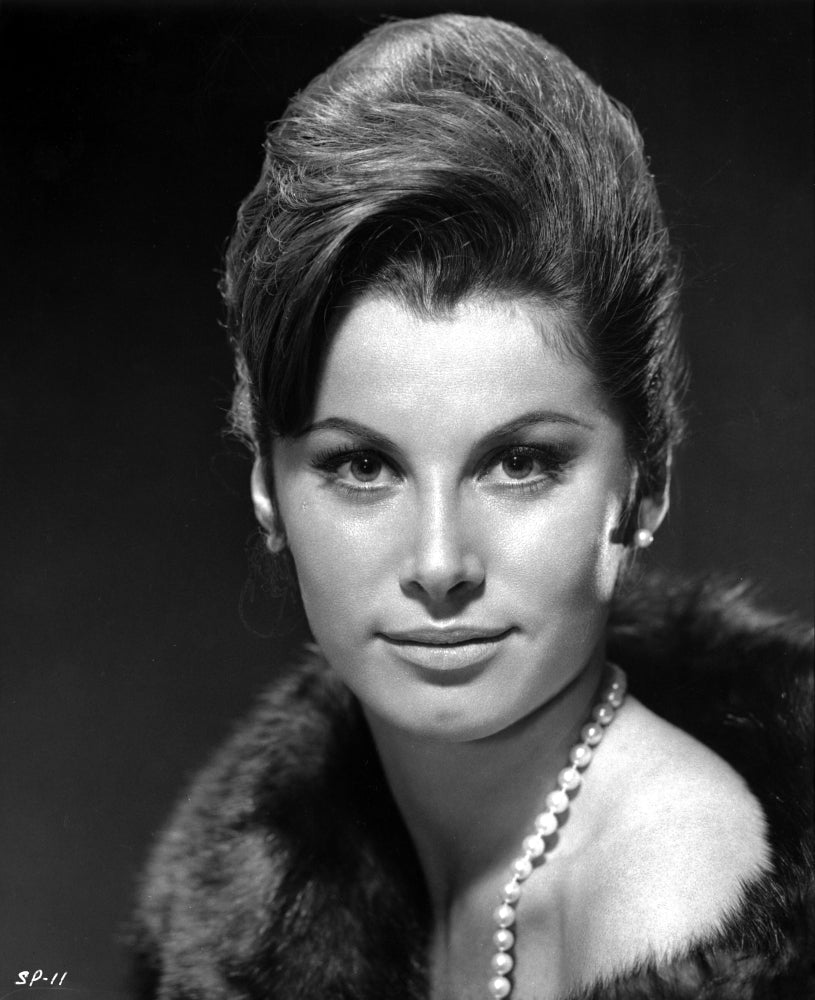 Black and white close-up portrait of Stefanie Powers wearing a fur coat and pearl necklace.