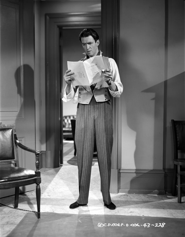 James Stewart reading a newspaper photo print in a white shirt and vest