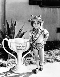 Shirley Temple photo print posed with oversized trophy in cute hat.