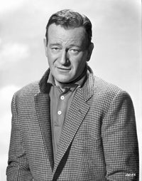Black and white photo portrait of John Wayne in a suit with a popped collar.