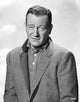 Black and white photo portrait of John Wayne in a suit with a popped collar.