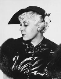 Mae West looking down in a glossy black dress with fur sleeves photo print.