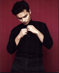Sebastian De Souza unbuttoning black shirt photo print against red background.