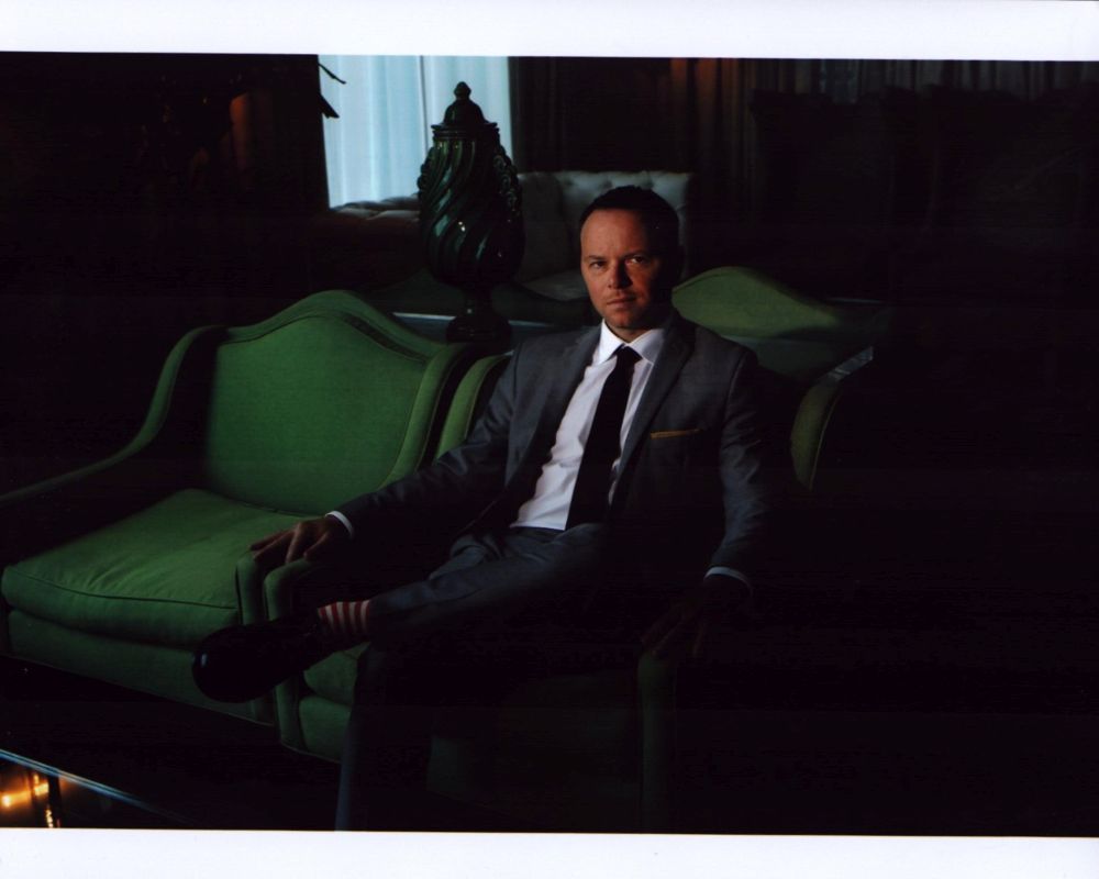 Noah Hawley seated in a suit on a green chair photo print.