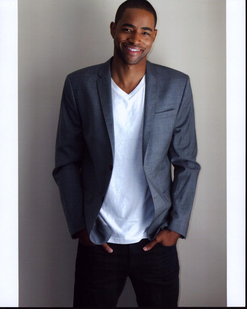 Jay Ellis in gray blazer photo print with hands in pockets.