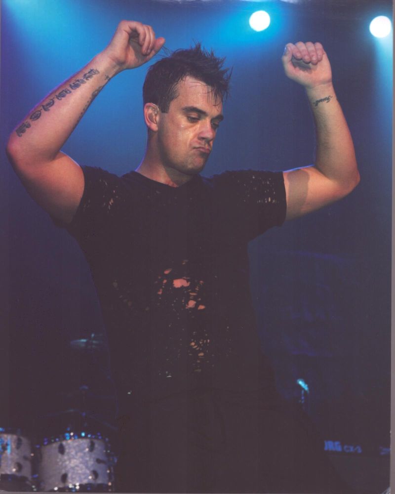 Robbie Williams on stage in ripped shirt with arms up photo print.