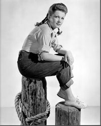 Black and white photo print of Anne Baxter sitting on wooden post.