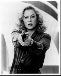 Black and white photo print of Kathleen Turner as V.I. Warshawski, showcasing her iconic pose with a gun.