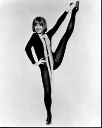 Shirley Maclaine black and white photo with leg up in long pearl necklaces.