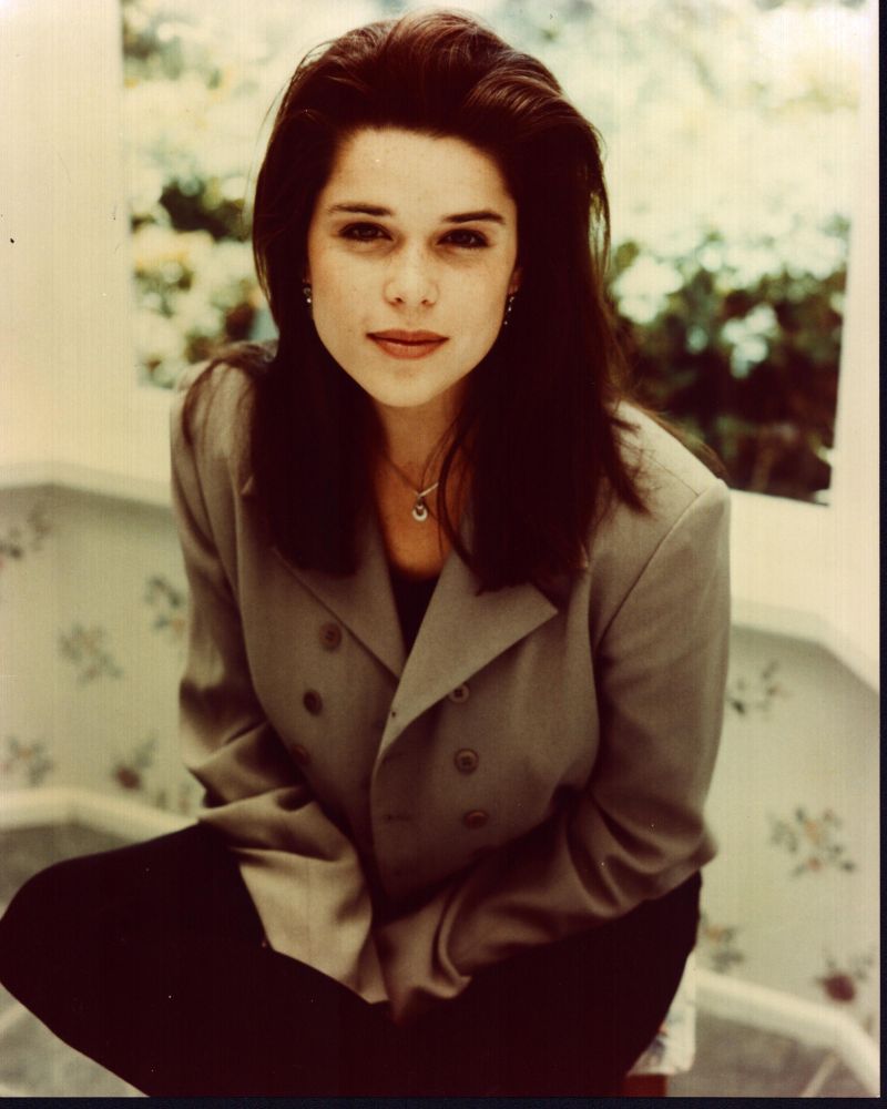 Neve Campbell seated in a tan blazer photo print.