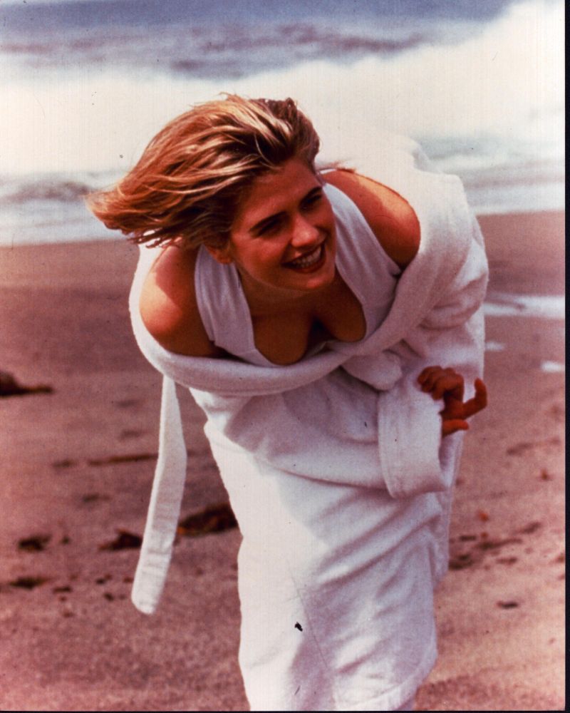 Kristy Swanson leaning forward on beach in white swimsuit and robe photo print