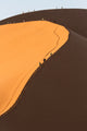 Hikers climbing a red sand dune in the Namib Desert poster print by Deborah Winchester.