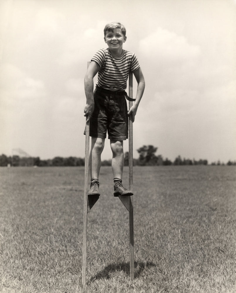 1930s-1940s print of a smiling boy on stilts wearing a striped shirt.