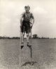 1930s-1940s print of a smiling boy on stilts wearing a striped shirt.