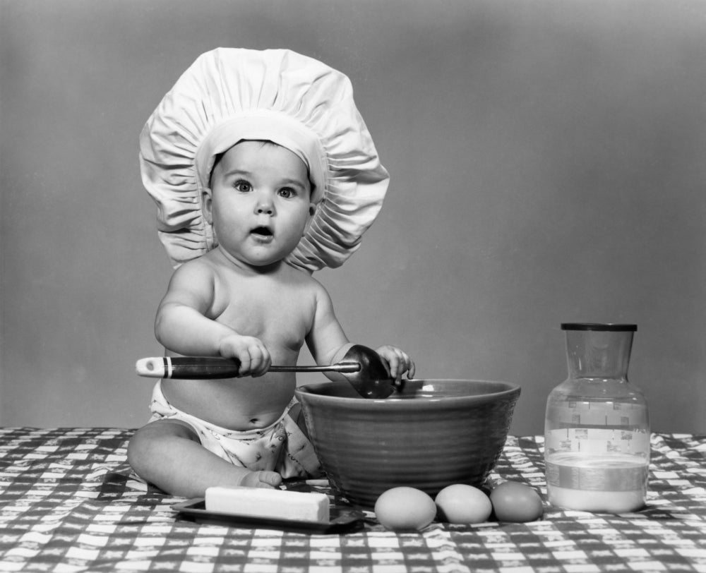 1960s baby in chef's hat mixing ingredients on checkered tablecloth