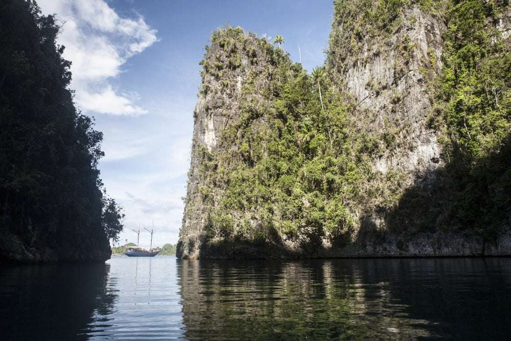 Rugged limestone islands framing an Indonesian pinisi schooner poster print.