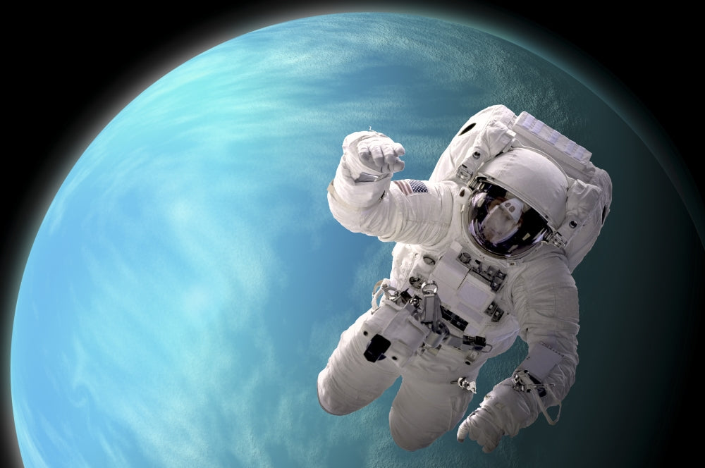 Astronaut floating in outer space poster print with a water-covered planet and nearby star.