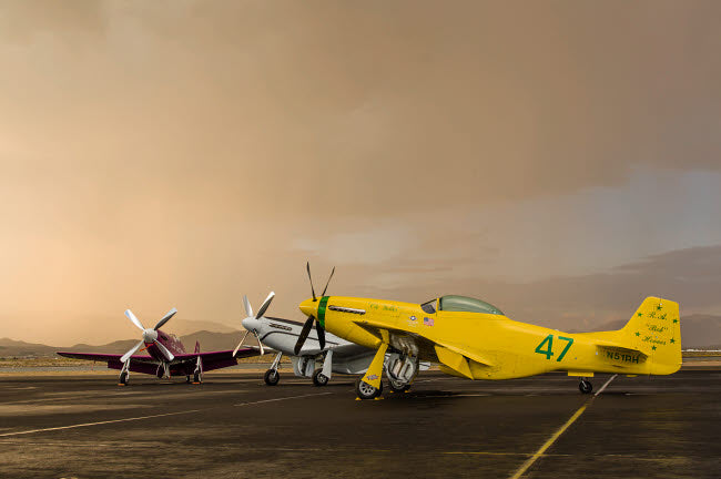 Three P-51 Mustangs parked on the ramp ahead of a storm poster print.