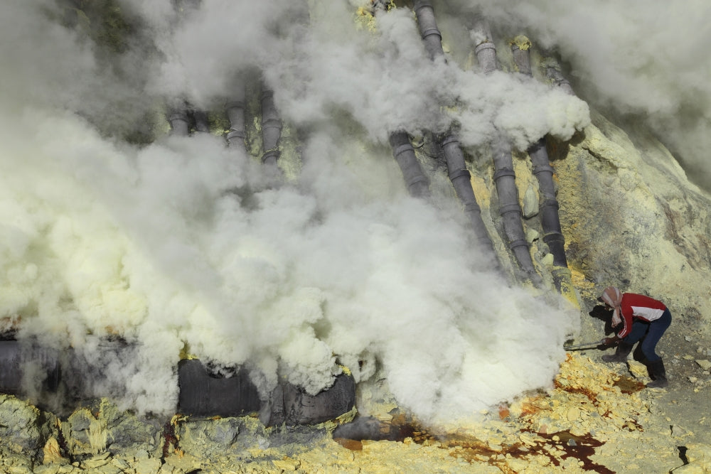 Miner breaking up sulfur deposits at Kawah Ijen Volcano in Indonesia poster print