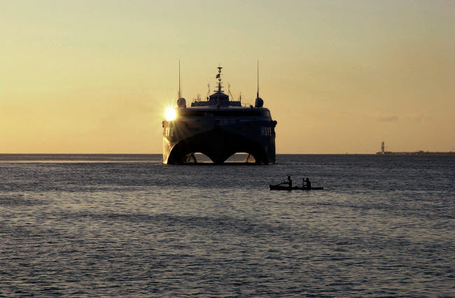 Fishermen canoeing past the US Navy contracted High Speed Vessel Two HSV-2 SWIFT poster print.