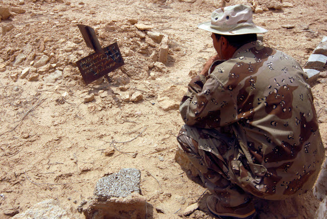 A resident reading the grave marker of an Iraqi soldier from the Iran and Iraq War.